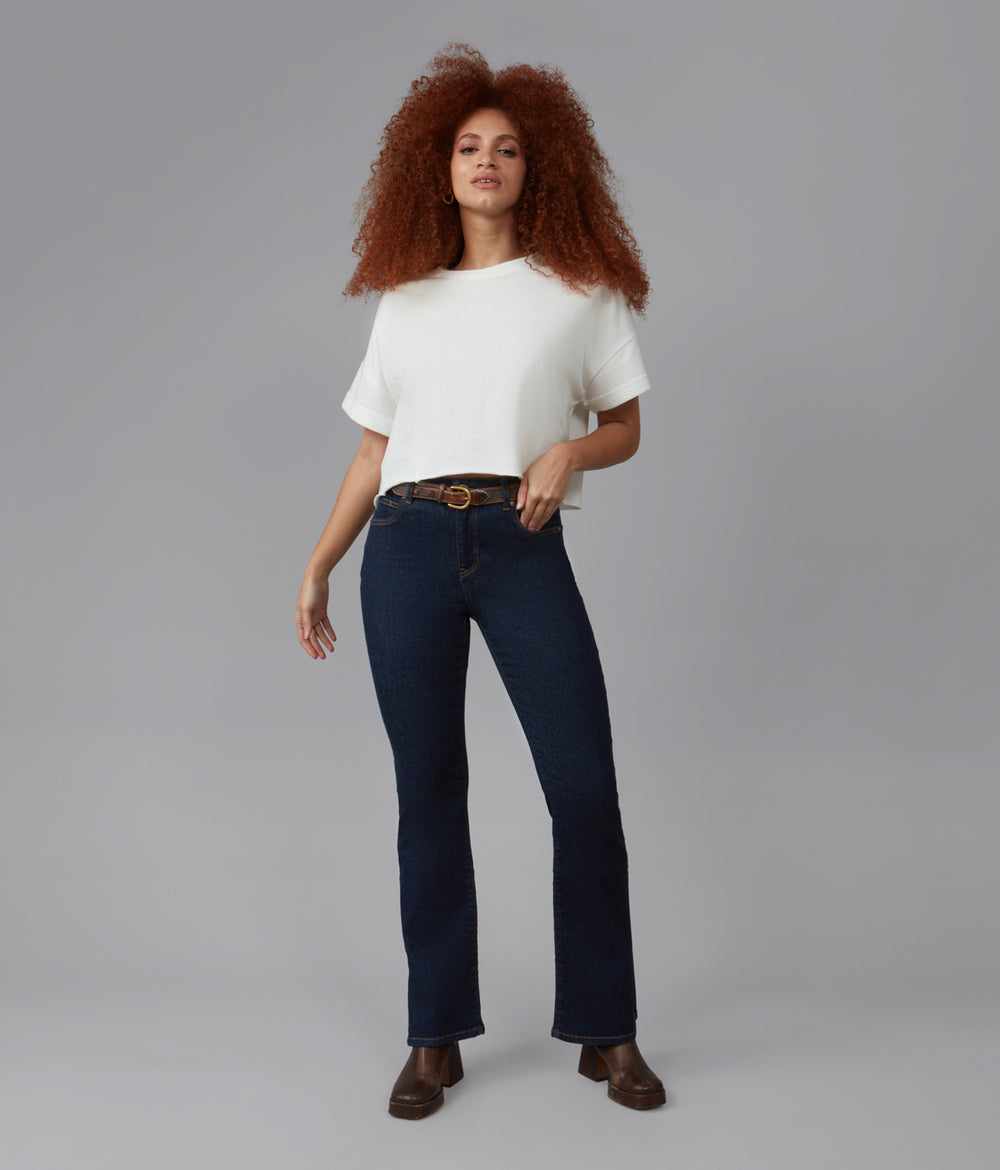 A female model wearing a white top and dark rinse blue jeans.